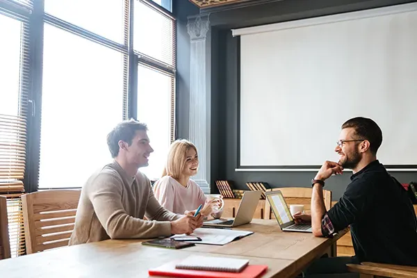 Three people in a room with laptops discussing ideas