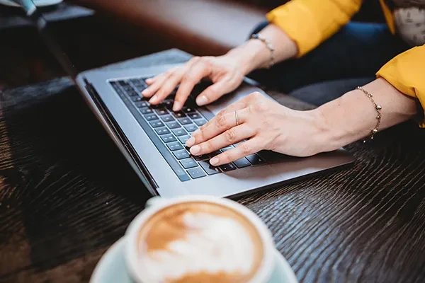 Person typing on laptop with coffee to their left