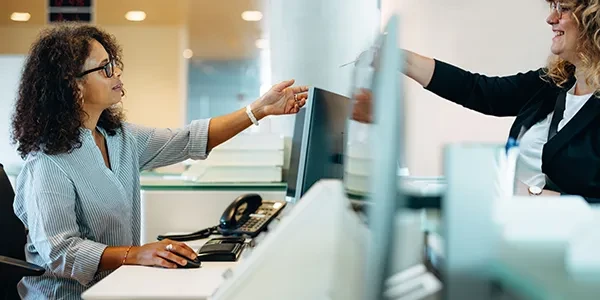 Woman receptionist with glasses being handed something by another woman