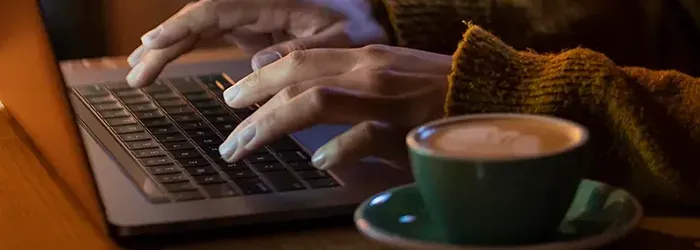Person typing on laptop with coffee mug