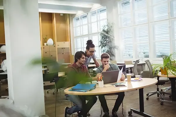 Three people looking at laptop while around a desk
