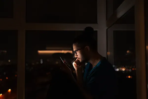 Man with glasses looking at mobile phone in dark