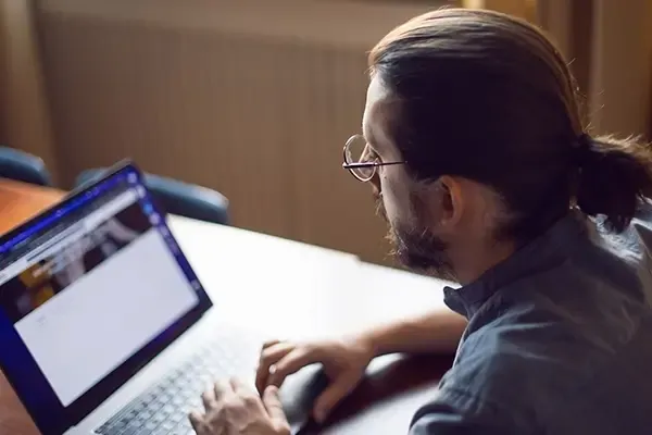 Man with glasses typing on laptop while sitting at table