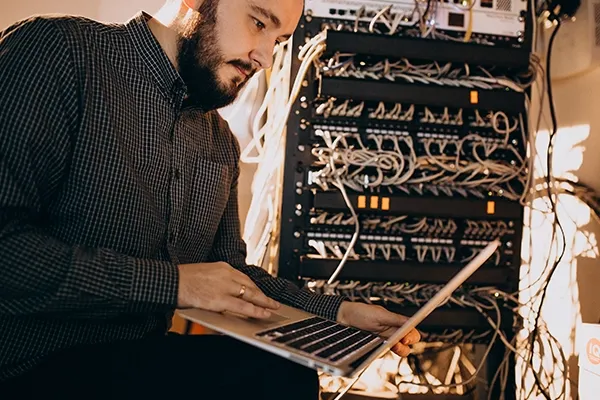 Man looking at laptop next to a server