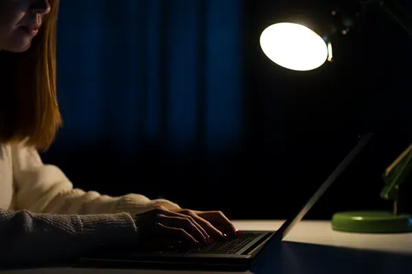 Woman typing in dark with light pointing at laptop