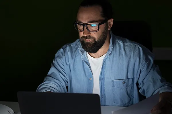 Man with glasses on looking at laptop in dark room