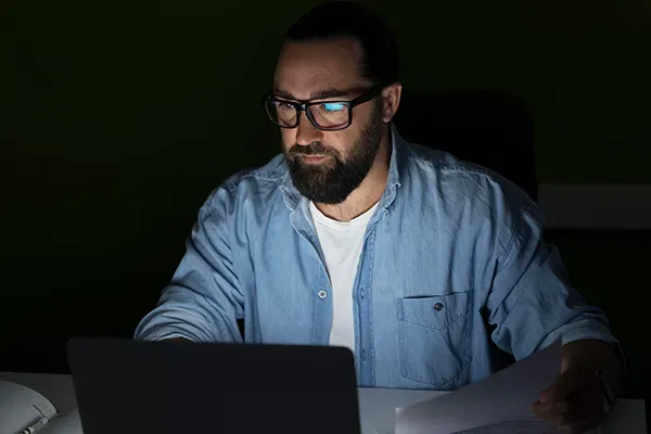 Man with glasses looking at laptop in the dark