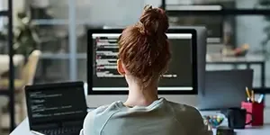 Back of woman looking at computer monitor with programming code