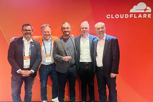 Group of men standing for a photo in front of red background with Cloudflare logo