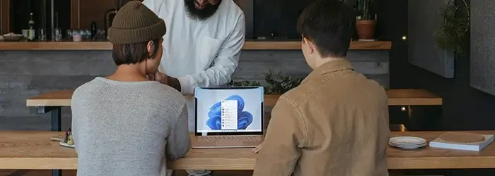 Three people looking around Windows laptop on table