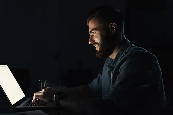 Man smiling in dark room while typing on laptop
