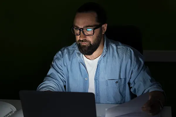 Man with glasses looking at laptop in the dark