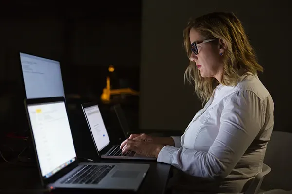 Woman with glasses looking down at laptop while typing