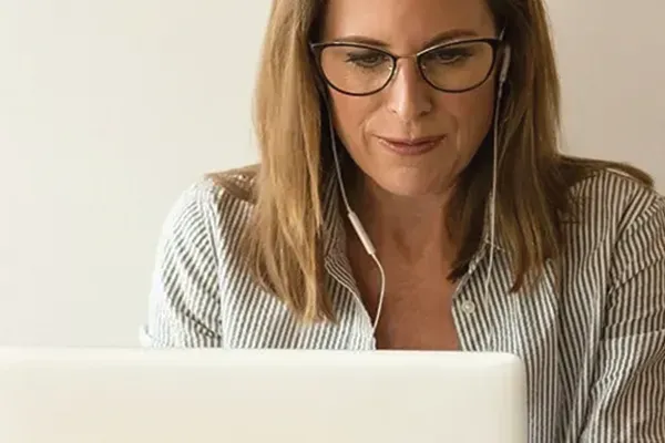Woman with glasses using laptop with earphones in