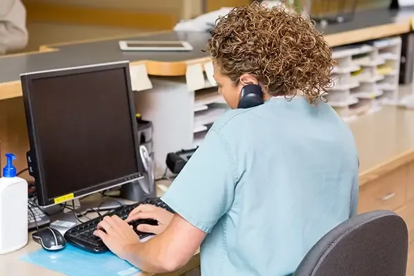 Female receptionist using telephone while typing on keyboard