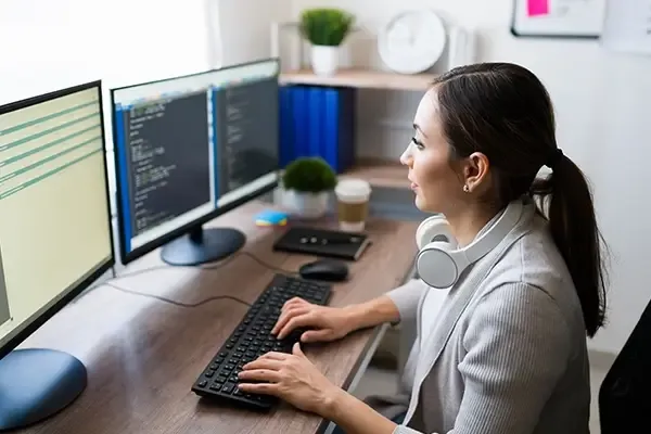Woman looking at monitors while typing out computer code