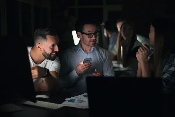 Three people talking in dark while holding mobile phone