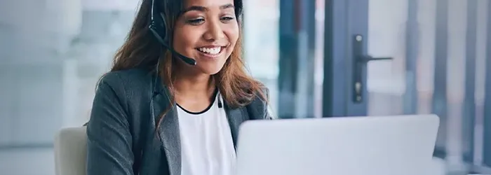 Woman smiling with headset on while looking at laptop