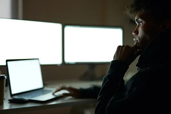 Woman looking at laptop and two monitors