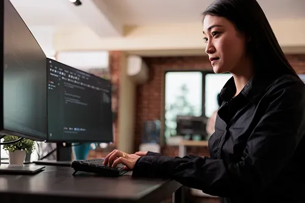 Woman looking at code on two monitors