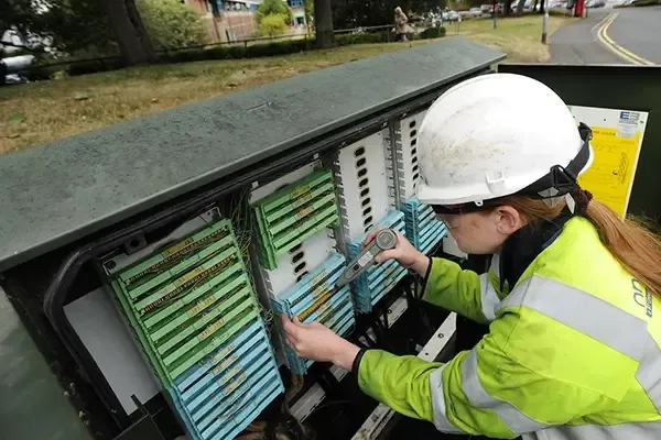 Woman with hard hat looking at broadband cabinet