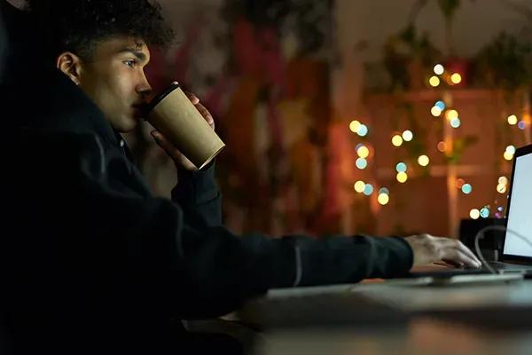 Man drinking coffee while typing on laptop