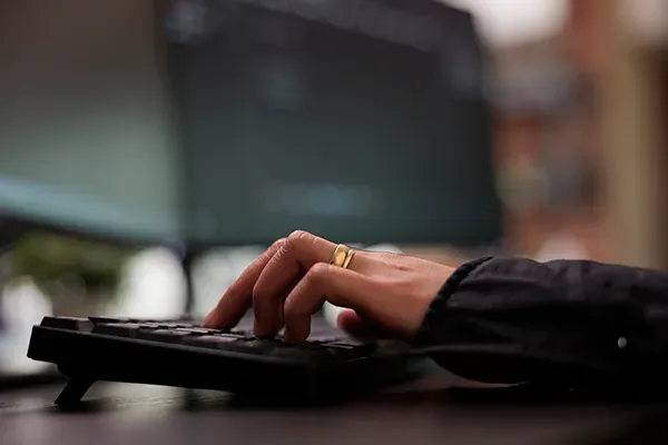 Close-up of person typing with two monitors in the background