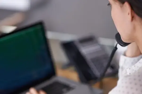 Woman holding handset to right ear while looking at laptop