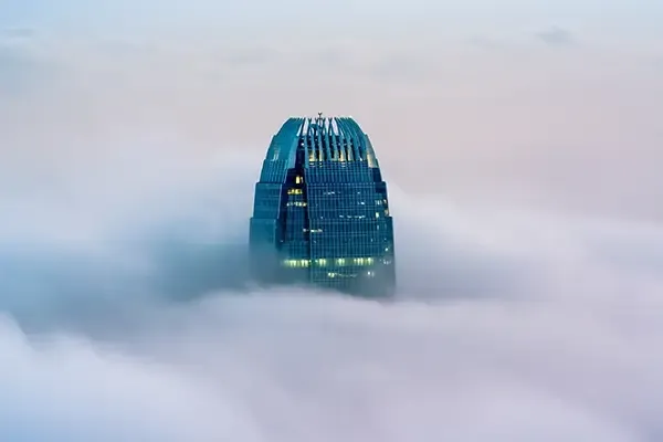 Glass skyscraper appearing above clouds