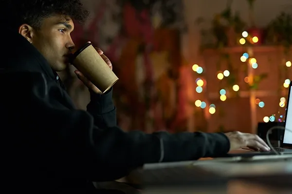 Man drinking coffee while typing on laptop