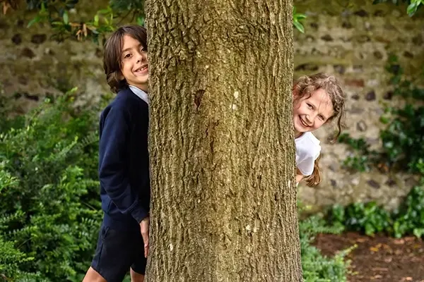 Two children hiding behind a tree