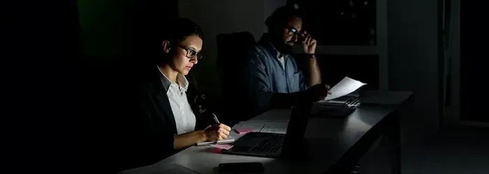 Man and woman with glasses sitting in dark room writing notes