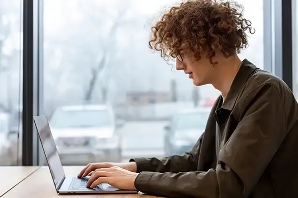 Man with glasses and curly hair looking down at laptop while typing on desk
