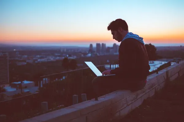 Man sitting on the edge of a wall with a laptop on lap