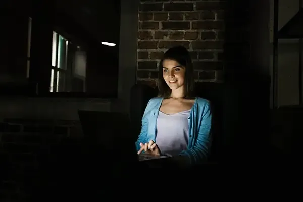 Woman smiling while using laptop in dark room