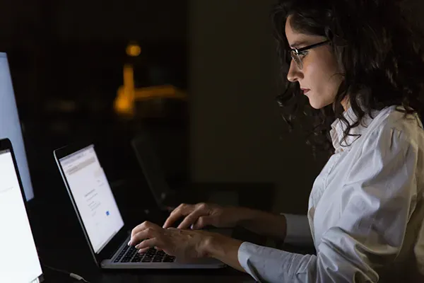 Side shot of woman with glasses looking down and typing on laptop