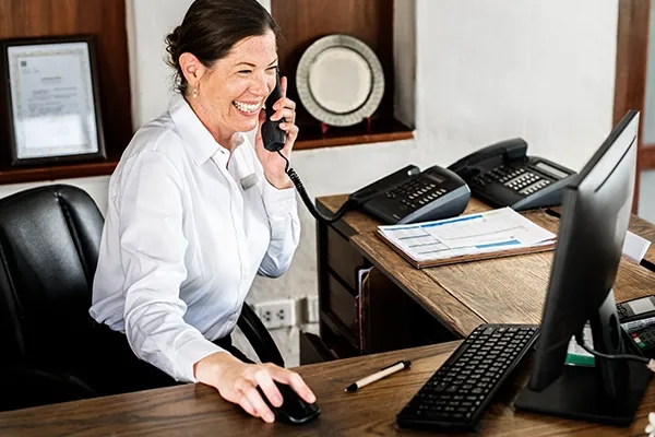 Woman smiling while holding telephone to left ear and using computer